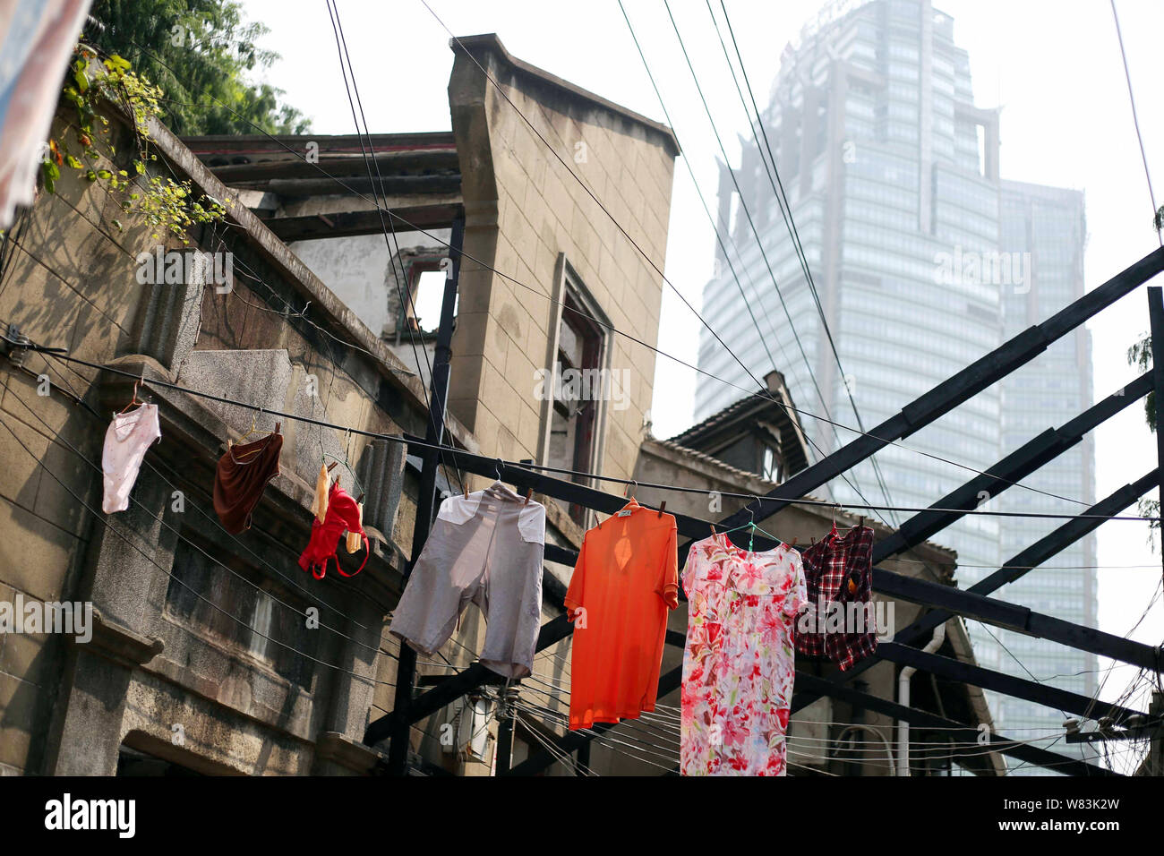 ------ Kleidung aufhängen an den Kabeln für die Trocknung über einen Weg zu einem Elendsviertel mit alten Häusern für den Wiederaufbau in Shanghai, China, 27 Ju demontiert werden Stockfoto