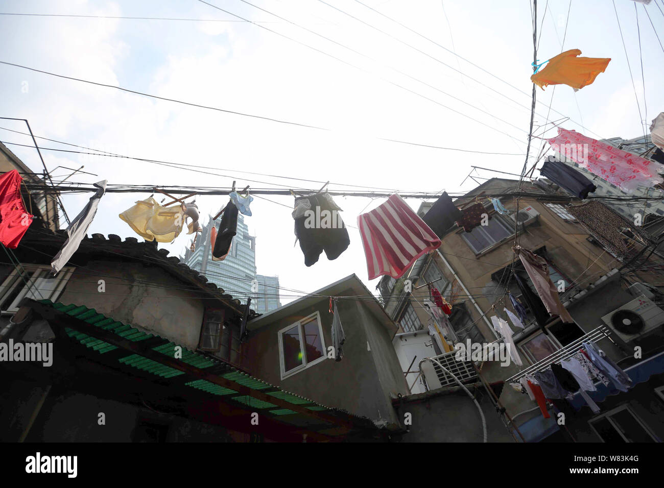 ------ Kleidung aufhängen an den Kabeln für die Trocknung über einen Weg zu einem Elendsviertel mit alten Häusern für den Wiederaufbau in Shanghai, China, 27 Ju demontiert werden Stockfoto