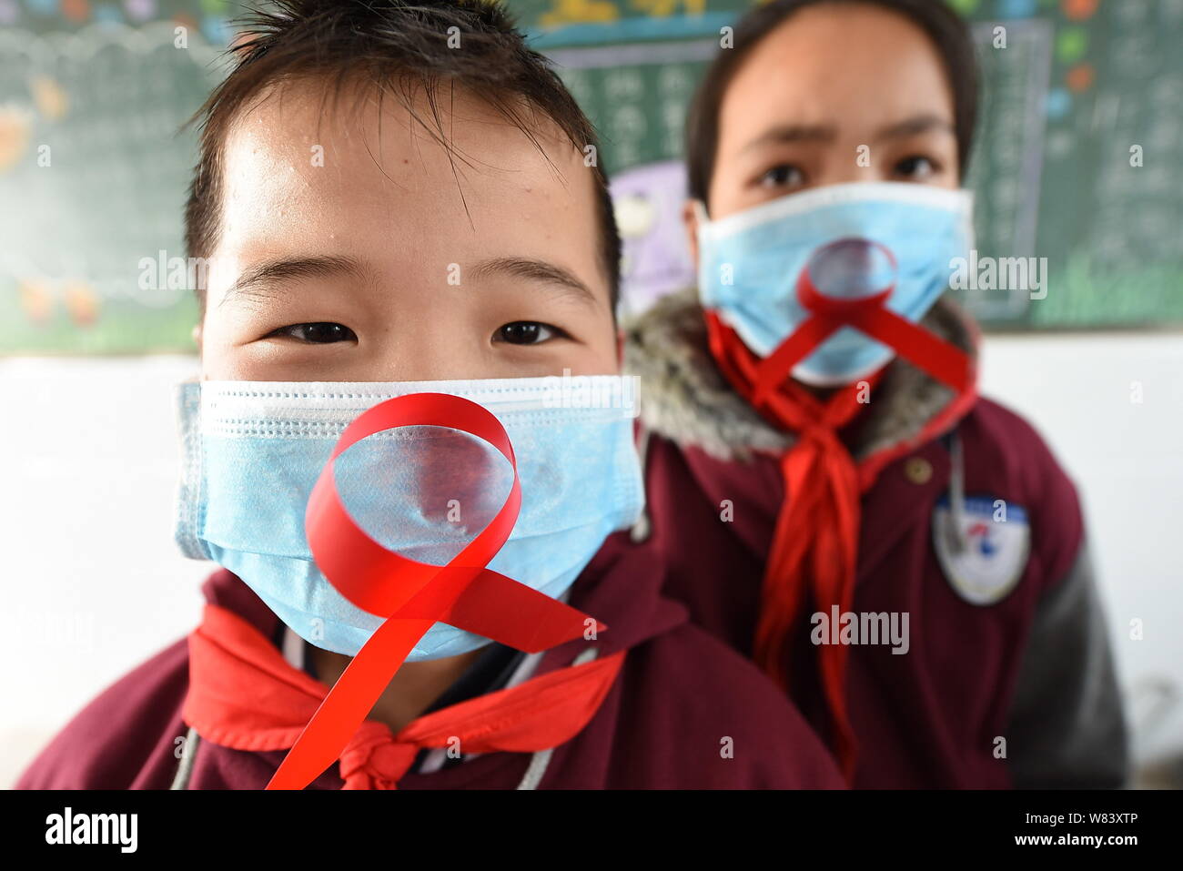 Junge chinesische Studenten tragen Gesichtsmasken zeigen rote Bänder, wie sie Vorbeugung von HIV und AIDS lernen Welt-AIDS-Tag im Klassenzimmer an eine Prim zu markieren Stockfoto
