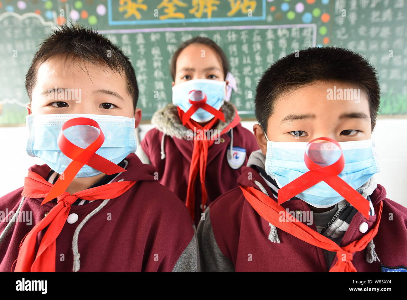 Junge chinesische Studenten tragen Gesichtsmasken zeigen rote Bänder, wie sie Vorbeugung von HIV und AIDS lernen Welt-AIDS-Tag im Klassenzimmer an eine Prim zu markieren Stockfoto