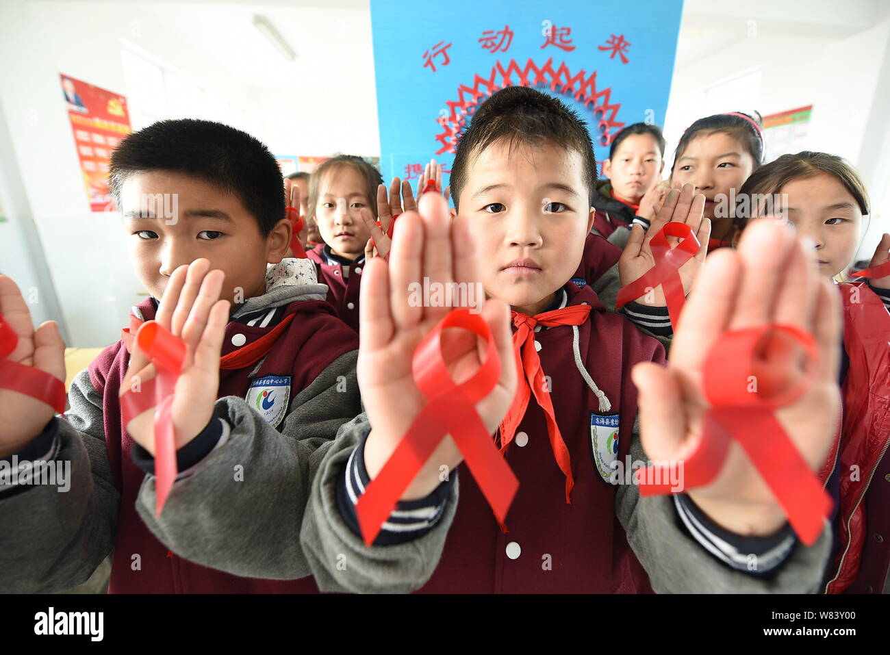 Junge chinesische Studenten zeigen rote Bänder, wie sie Vorbeugung von HIV und AIDS lernen Welt-AIDS-Tag im Klassenzimmer an einer Grundschule in Linia zu markieren Stockfoto