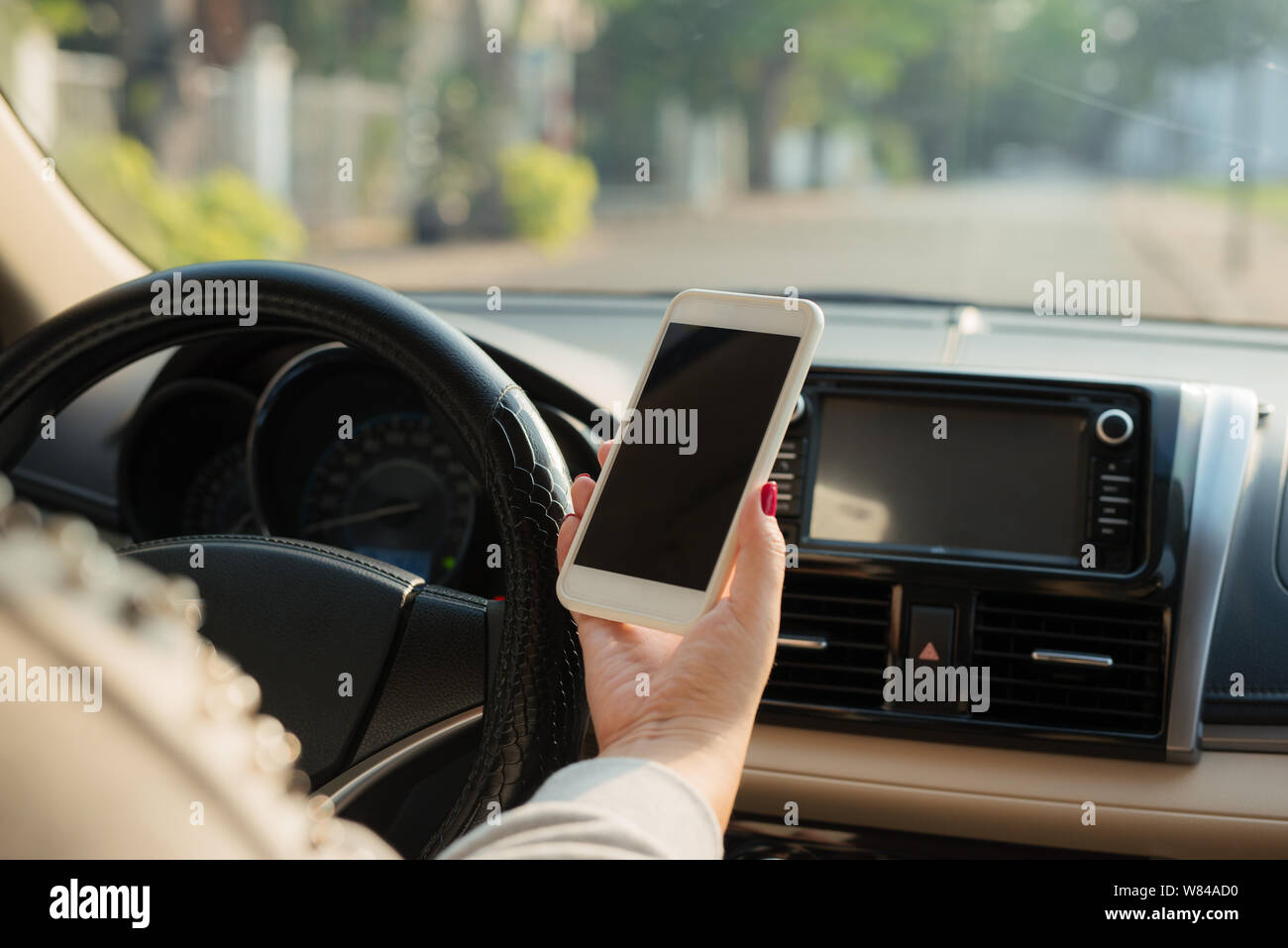 Junge Fahrerin mit Touch-Screen-Smartphone und Hand halten Lenkrad im Auto. Stockfoto