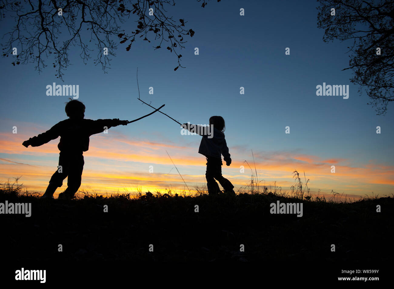 Kleine Kinder spielen mit einem Stick Kampf am Rande des Waldes bei Sonnenuntergang, Norfolk, Dezember 2010. Model Released. Stockfoto