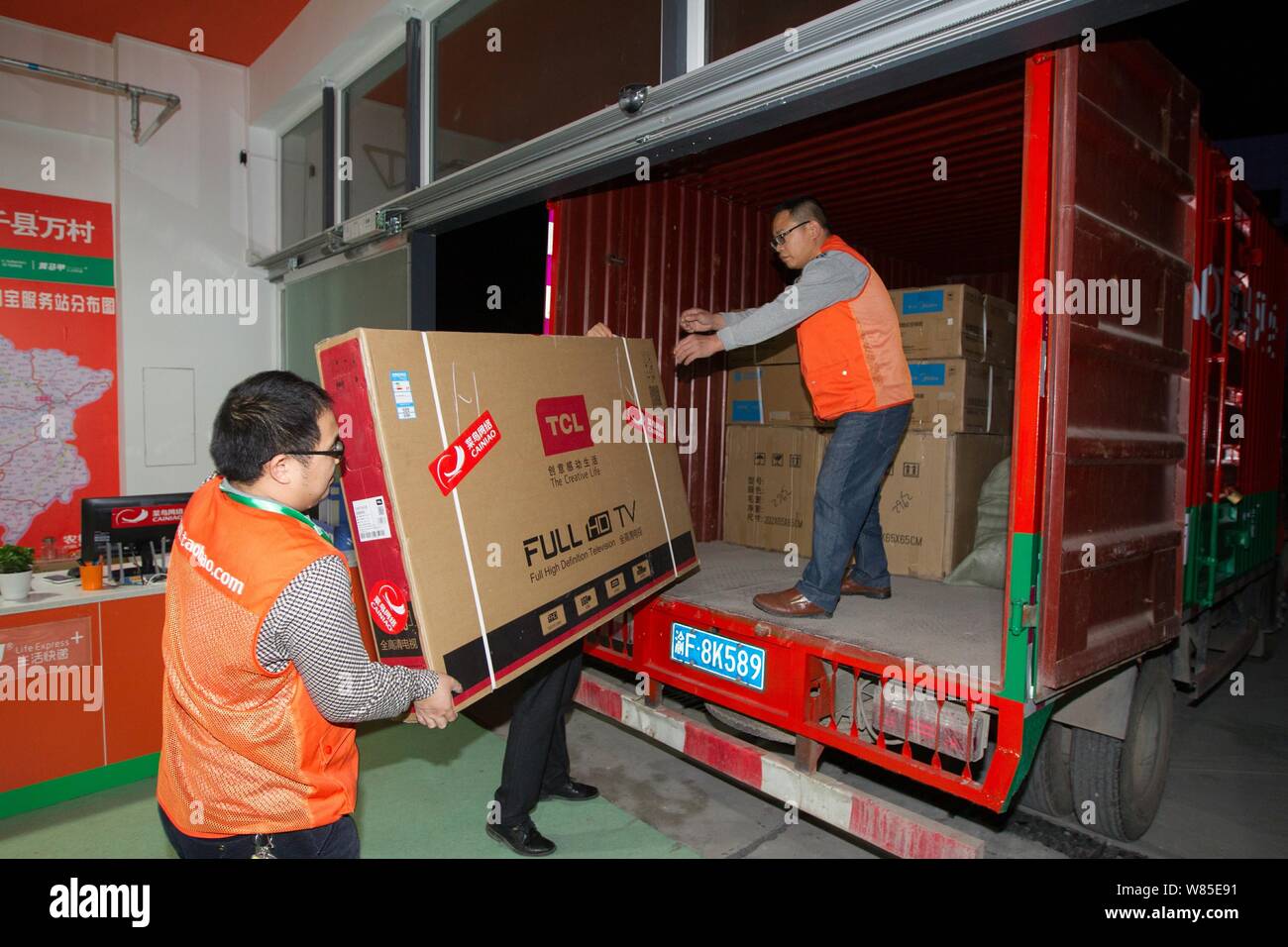 ---- Chinese Kuriere von Alibaba Logistikdienstleistungen Cainiao Netzwerk einen Fernseher auf einen Van laden an einer Tankstelle von cun.taobao.com, Al unterstützt. Stockfoto