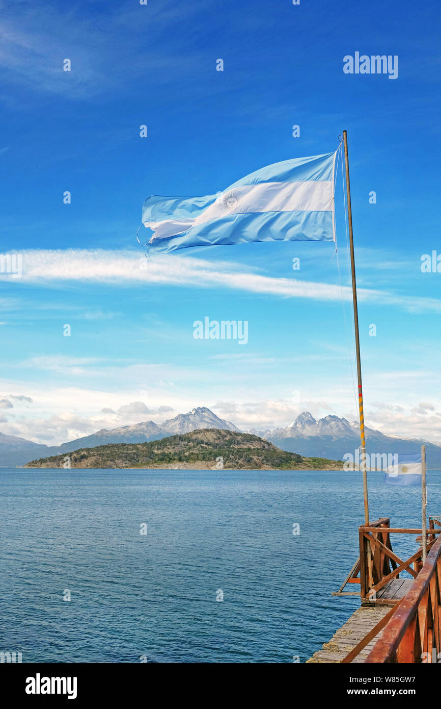 Panoramablick auf die argentinische Flagge gegen die patagonischen Berge und kleine Inseln von grüner Vegetation bedeckt, hinter dem blauen Wasser des B Stockfoto