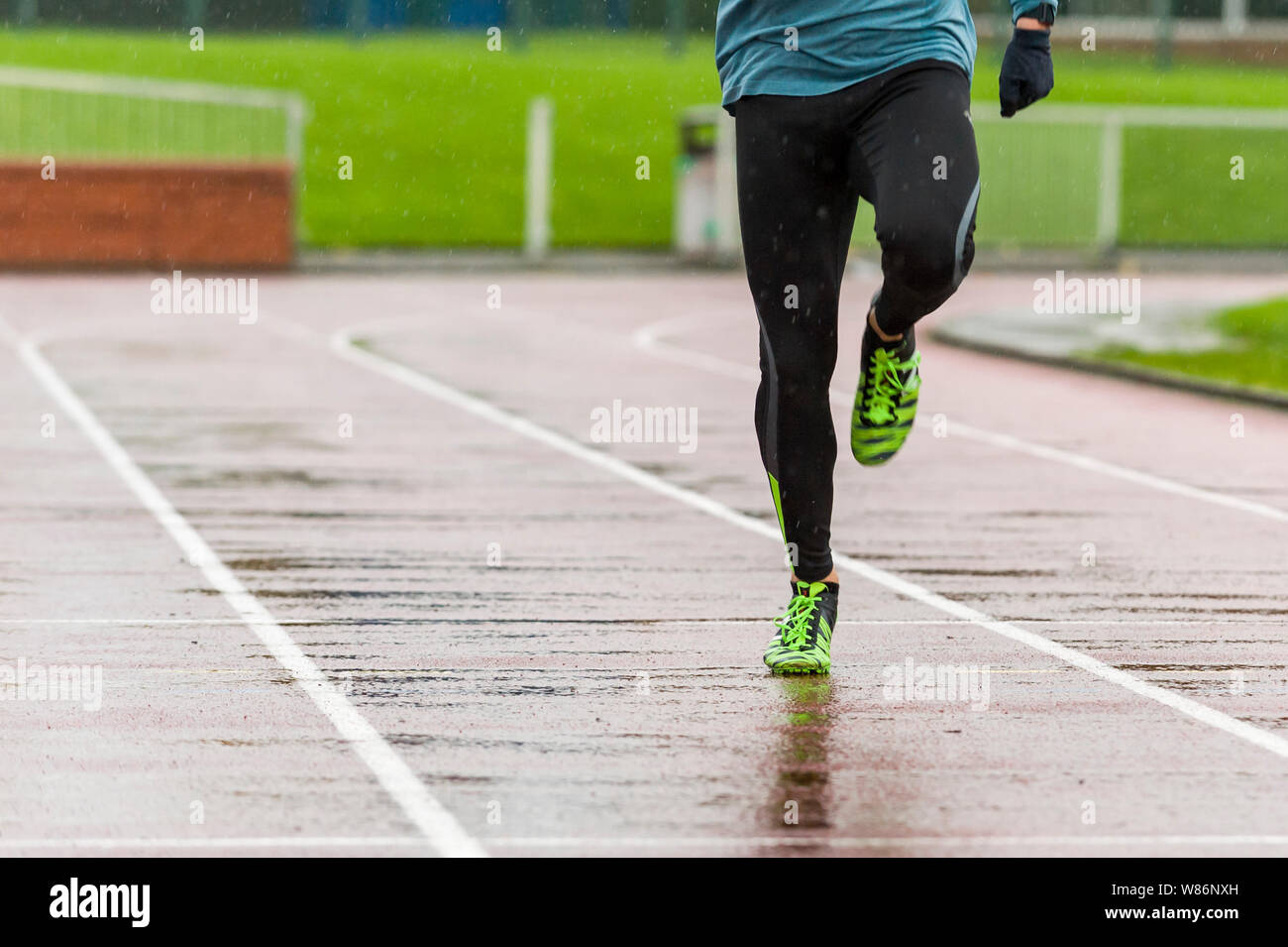 Männliche Athlet Running und Training auf einer Leichtathletikbahn an einem regnerischen Tag. Im Bild von der Taille abwärts die Aufmerksamkeit auf die Beine zu ziehen. Stockfoto