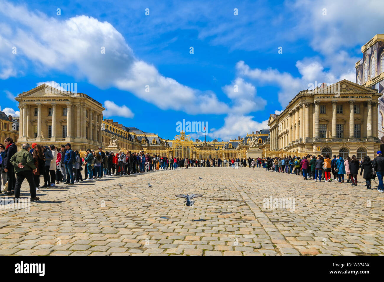 Tolle Aussicht auf eine große U-förmige Schlange der Besucher vor dem Schloss von Versailles im Golden Royal Tor im gepflasterten Hof der Ehre... Stockfoto