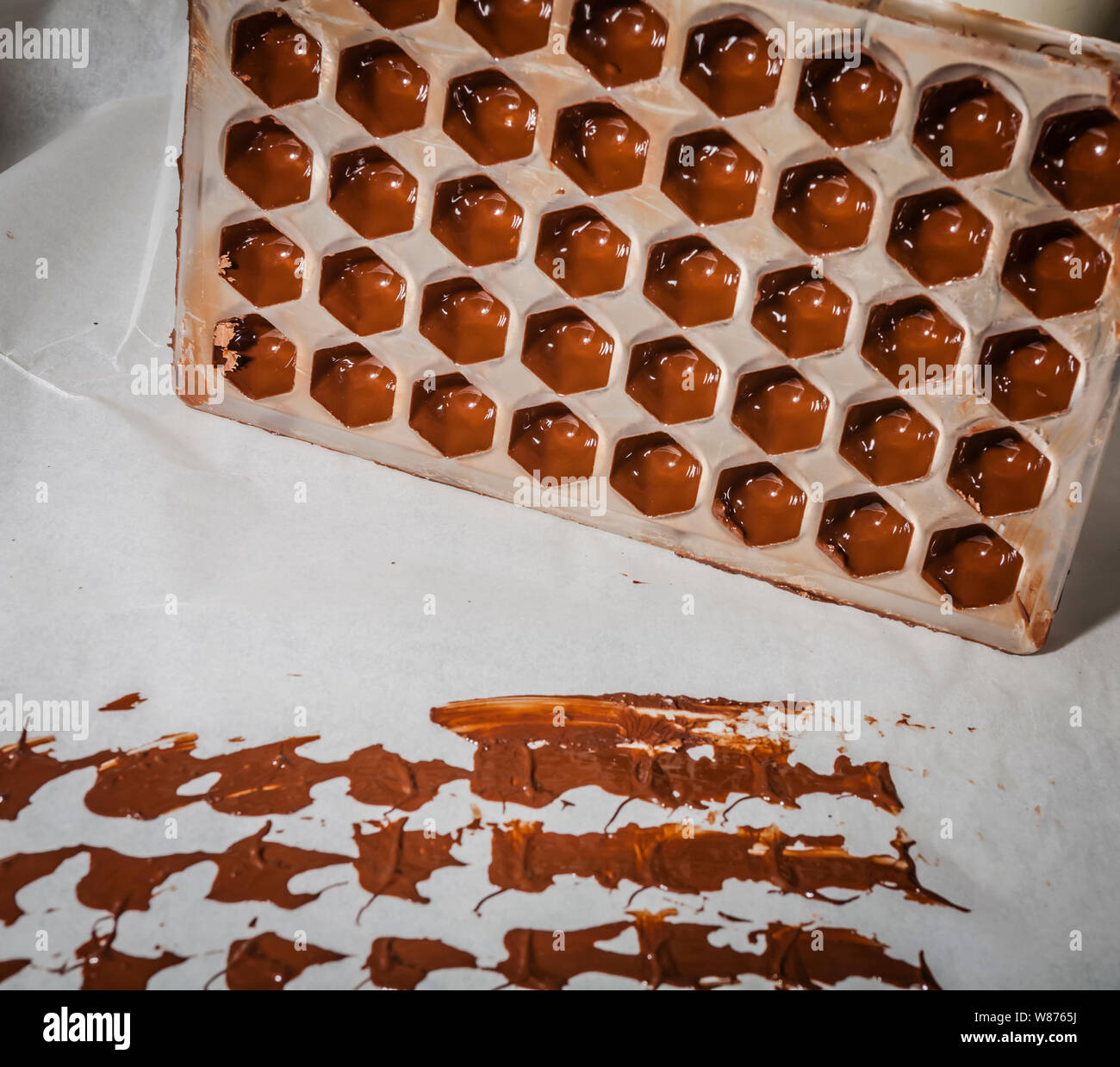 Ein Werkzeug für die Herstellung von Pralinen voll von geschmolzener Schokolade mit Schokolade Marken auf dem Papier Stockfoto