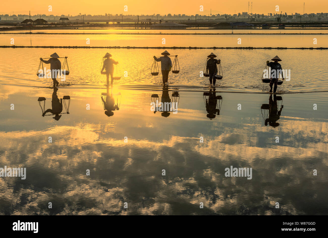 Frau Arbeiter die Körbe der frisch geerntete Salz auf ihren Schultern in Hon Khoi Salz Feld bei Sonnenaufgang, Nha Trang Provinz, Vietnam Stockfoto