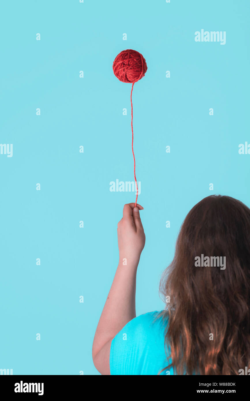 Seltsame Kindheit Konzept mit einer Frau mit einem schwebenden roten Faden Kugel wie ein Ballon. Sonderbar stricken Handarbeiten Konzept. Minimale Kindheit frame Stockfoto