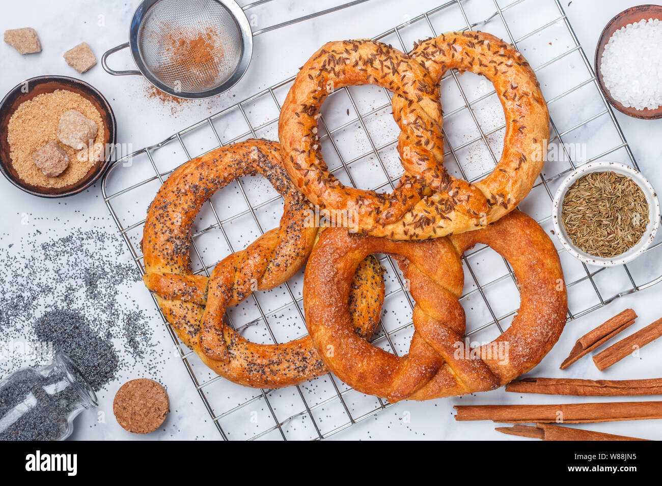 Brezel. Frisch gebackene Brezeln mit Zucker, Mohn, Zimt und Kreuzkümmel. Köstlichen hausgemachten süßen und salzigen Backwaren und Zutaten auf den Tisch. Stockfoto