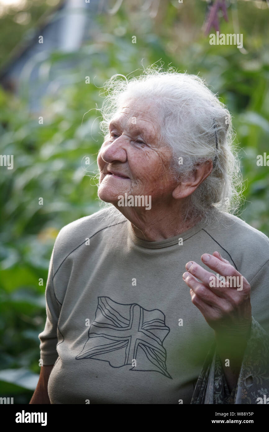 Nahaufnahme Porträt einer alten Frau mit grauem Haar hängt Kleidung auf einem trocknen, verschwommenen Hintergrund einer grünen Wiese, selektiven Fokus Stockfoto