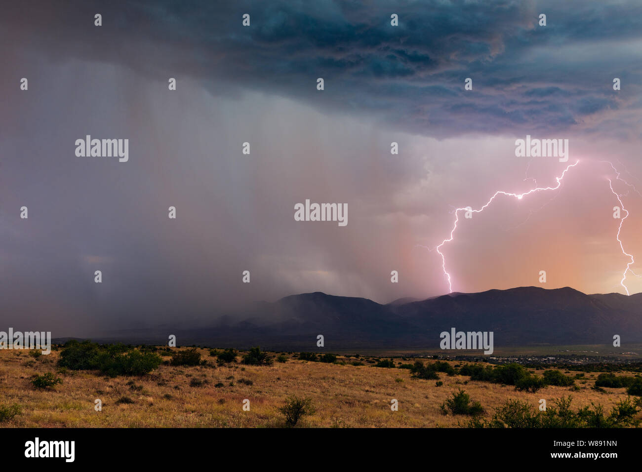 Ein Blitz bei Sonnenuntergang trifft den Mingus Mountain, als sich ein Monsunwetter mit starkem Regen über das Verde Valley in der Nähe von Cottonwood, Arizona, USA, bewegt Stockfoto