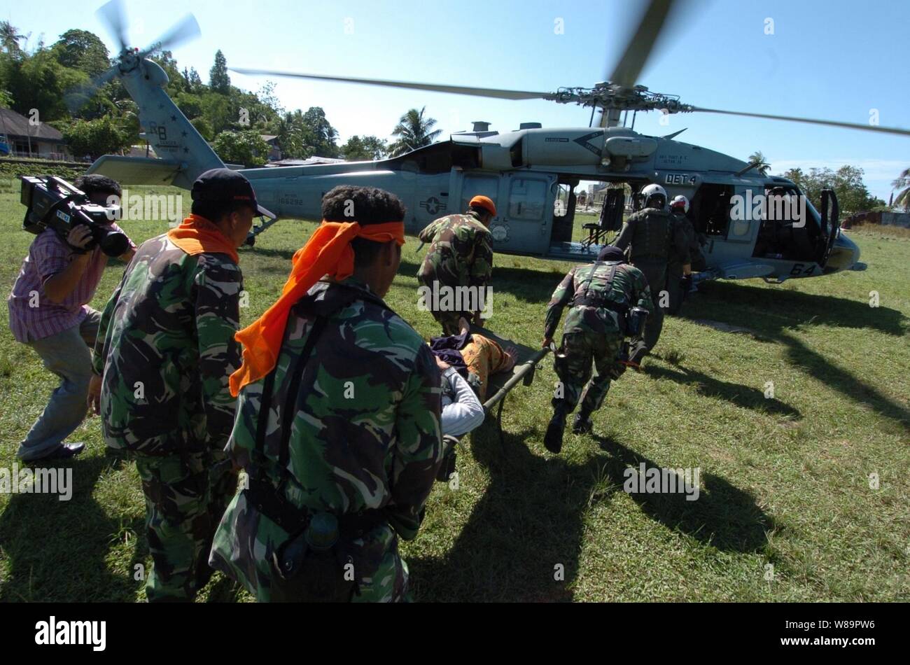Indonesische Soldaten führen eine indonesische Frau zu einem wartenden U.S. Navy MH-60 Knighthawk Helikopter für ihren Hilfsfluegen aus Nias, Indonesien, zum Krankenhaus ship USNS Mercy (T-AH 19) am 6. April 2005. Barmherzigkeit und der Bekämpfung der Stores ship USNS Niagara Falls (T-AFS 3) Derzeit vor der Küste von Nias, die medizinische und humanitäre Hilfe für die Opfer des 28. März 2005, 8,7-Erdbeben. Der Hubschrauber und die Crew sind zu Helicopter Combat Support Squadron 5 an Bord der Niagara Falls zugeordnet. Stockfoto