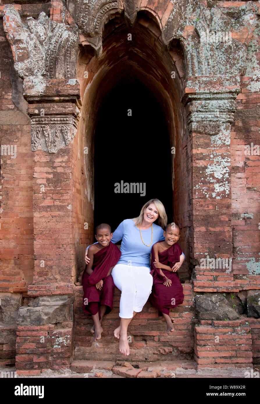 Ein kaukasischer weiblichen Touristische und Zwei birmanischen buddhistischen Novizen in einem antiken Tempel lachend an Kamera in Bagan Myanmar und Touristische freigegeben wird. Stockfoto