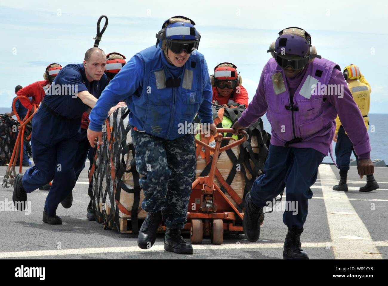Us-Marine Seeleute an Bord des US-amerikanischen 7 Flotte Flaggschiff USS Blue Ridge (LCC 19) Paletten der humanitären Hilfe und Katastrophenhilfe Kits über den shipís Flight Deck während eines laufenden Auffüllung mit der Flotte Auffüllung öler USNS Rappahannock (T-AO 204) im Südchinesischen Meer am 12. März 2011. Die Blue Ridge geladen die Kits, um sicherzustellen, dass die Crew bereit war, zur Unterstützung der Erdbeben und Tsunami Hilfsaktionen in Japan, wie verwiesen. Stockfoto
