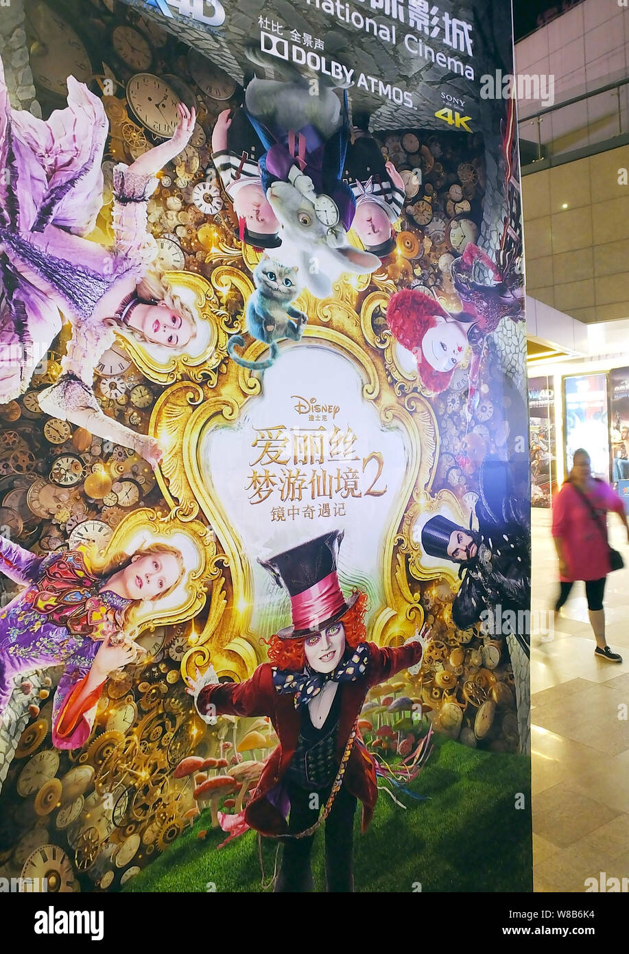 Eine Chinesische filmgoer Spaziergänge hinter einem Plakat des Films "Alice Through the Looking Glass" in einem Kino in Yichang, Provinz Hubei, China 25. Stockfoto
