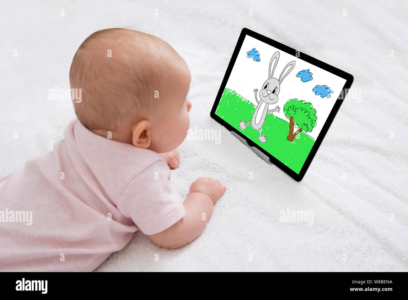 Ein kleines Baby liegt auf dem Teppich und sich Zeichentrickfilme auf digitalen Tablet Stockfoto