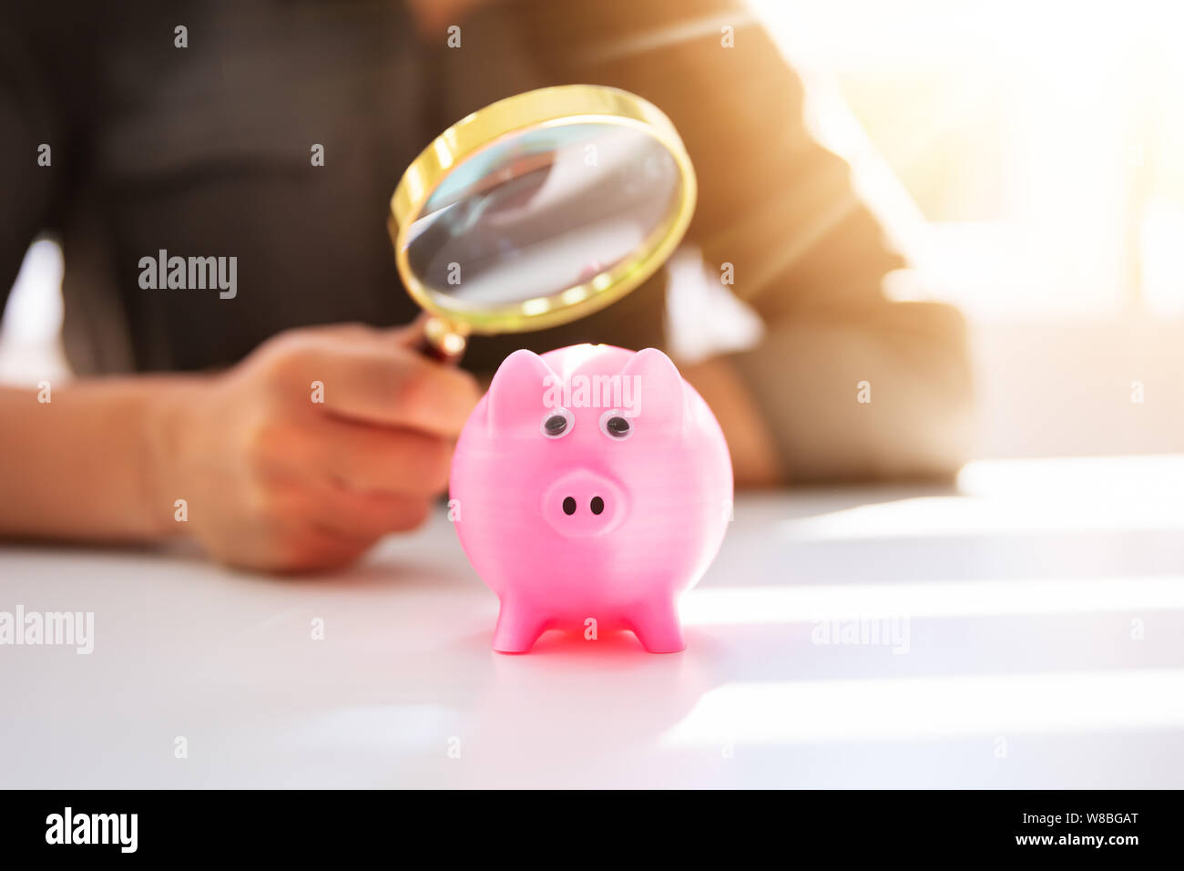 Nahaufnahme einer Geschäftsfrau, Prüfung der rosa Sparschwein durch Lupe auf weißem Schreibtisch Stockfoto