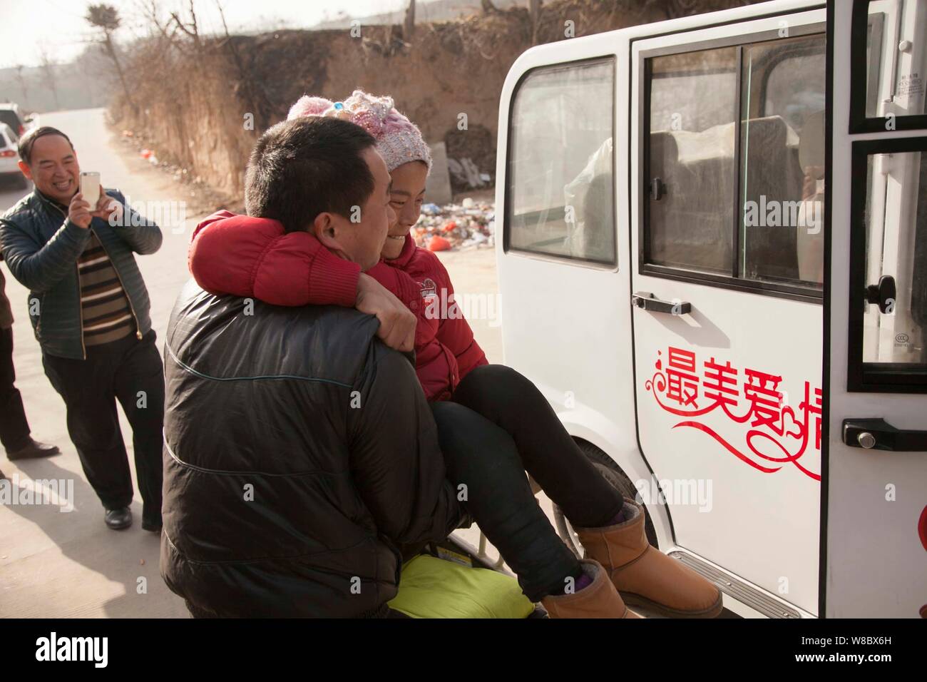 ------ Chinesischer Bauer Ma Xiaopeng, front, trägt seine gelähmte Frau Zhang Guilin auf ein Fahrzeug von einem Unternehmen gespendet vor ihrem Versand an Stockfoto