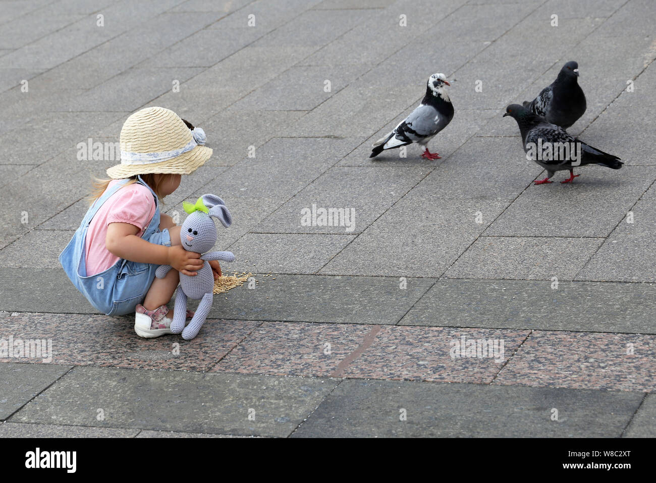 Kind füttern Tauben, kleine Mädchen spielen auf einer Straße der Stadt. Glückliche Kindheit, Sommer Freizeitaktivitäten, Kind und Vögel Stockfoto