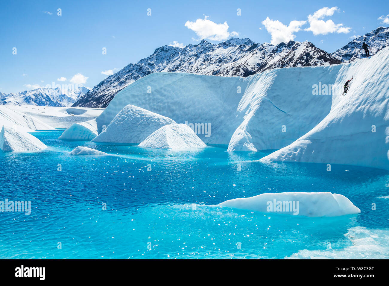 Ice climber aufsteigend eine Wand aus Eis in Richtung ihrer Kletterführer, vor einem tiefblauen See auf der Matanuska Gletscher in Alaska. Stockfoto