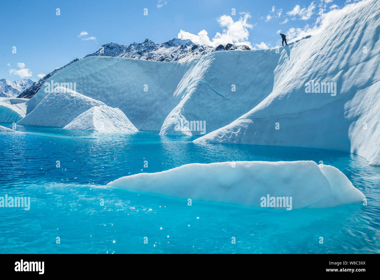 Junger Mann auf einem großen Felsen auf der Matanuska Gletscher in Alaska. Unterhalb der Wand aus Eis ist ein Deep Blue Pool oder Supraglazialen See auf dem glacie Stockfoto