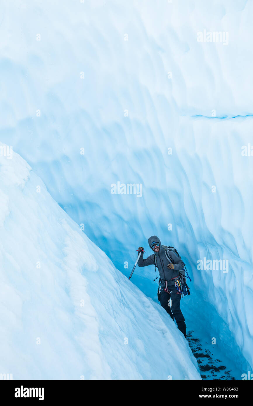 Fröhliche Eisklettern Führung zu Fuß durch die engen abfallende Schlucht auf der Matanuska Gletscher. Er geht durch einen flachen Fluss, der den Canyon aus th Schnitt Stockfoto