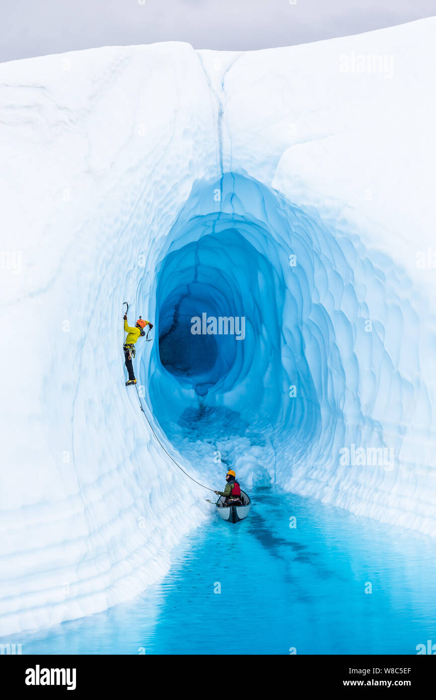 Ice climber, die den außerhalb einer Eishöhle auf der Matanuska Gletscher. Die große Höhle wird von einem Supraglazialen See, oder blauen Pool überschwemmt, auf der Sur Stockfoto