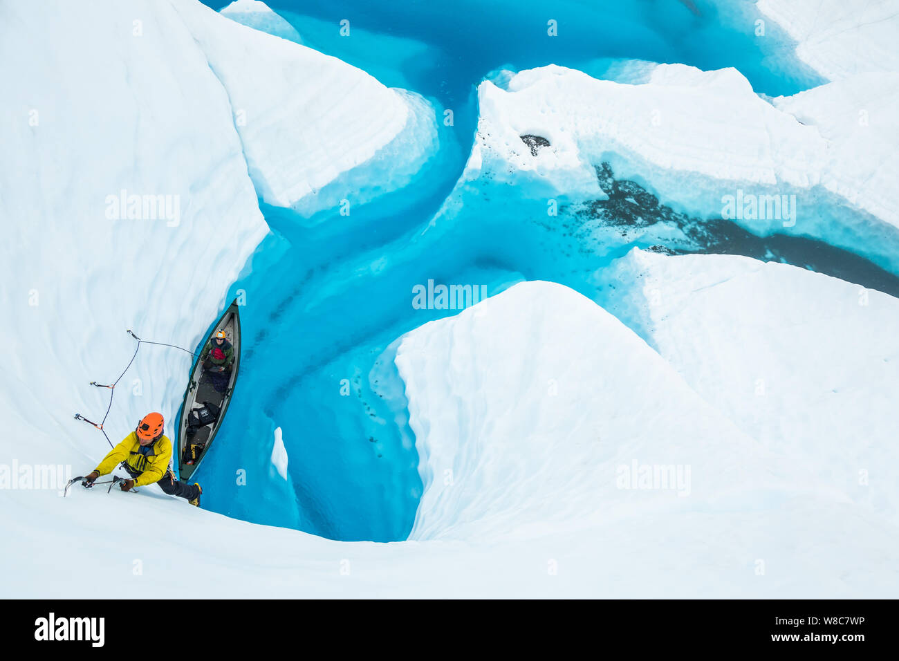 Ice climber in Gelb und Orange, die ein Eis Aufstieg aus ein Kanu auf einem blauen Pool auf der Matanuska Gletscher. Stockfoto
