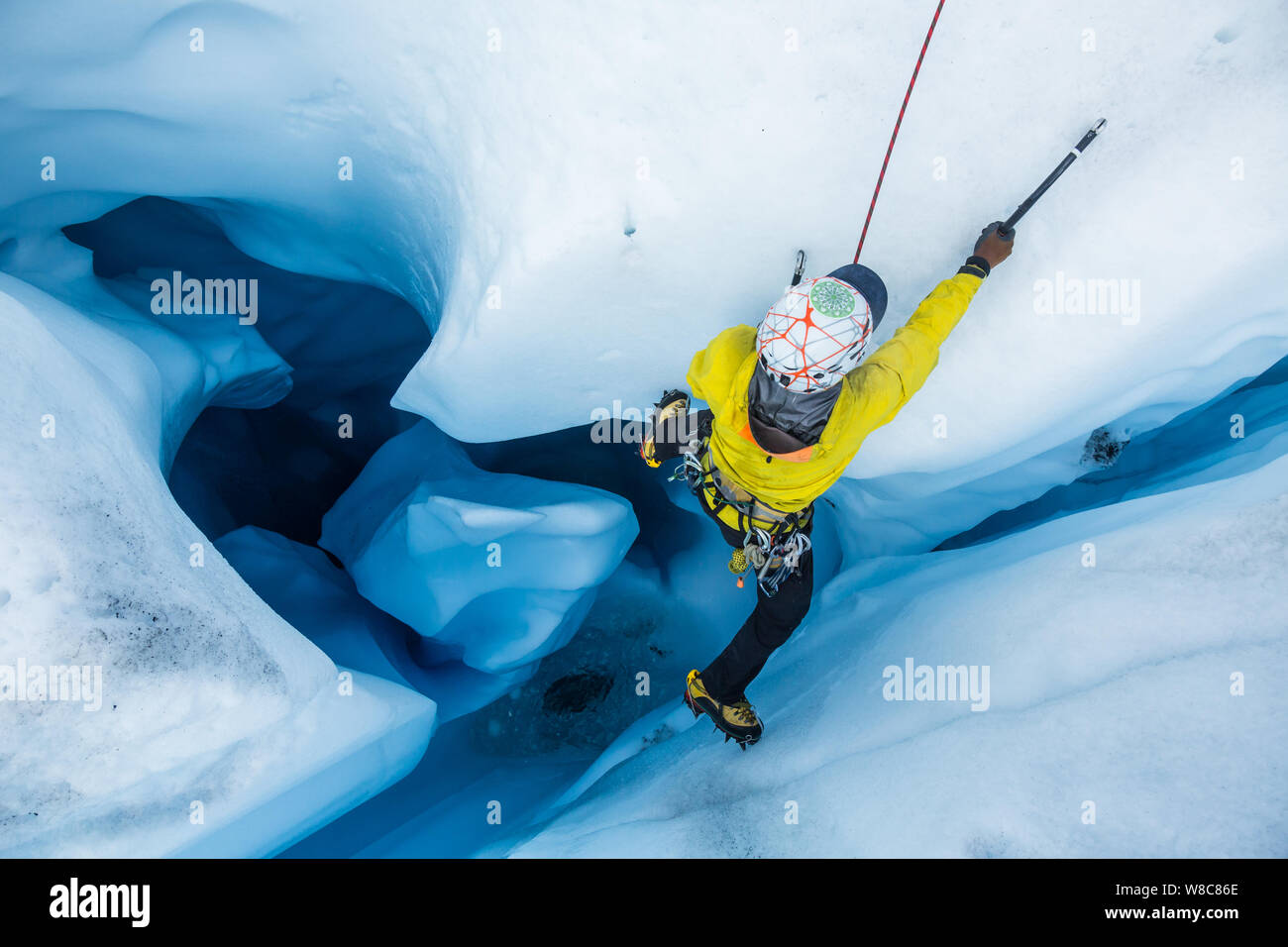 Ice climber von oben, als er aus einer vertikalen Moulin im Gletschereis klettert. Wasser aus dem schmelzenden Matanuska Gletscher Schnitte interessante Formationen Stockfoto