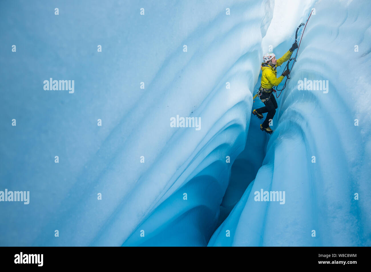 Ice climber abgesenkt in schmale Eis Canyon auf der Matanuska Gletscher. Er klettert zwischen Wänden von seltsamen wellenförmige Muster im Eis geschnitzt von einem Fluss von Stockfoto