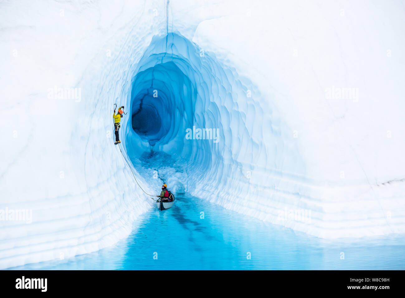 Eiskletterer ein Aufstieg aus dem Kanu vor einer Eishöhle. Die Höhle ist von einem großen blauen See auf der Oberfläche der Matanuska Gletscher überflutet i Stockfoto