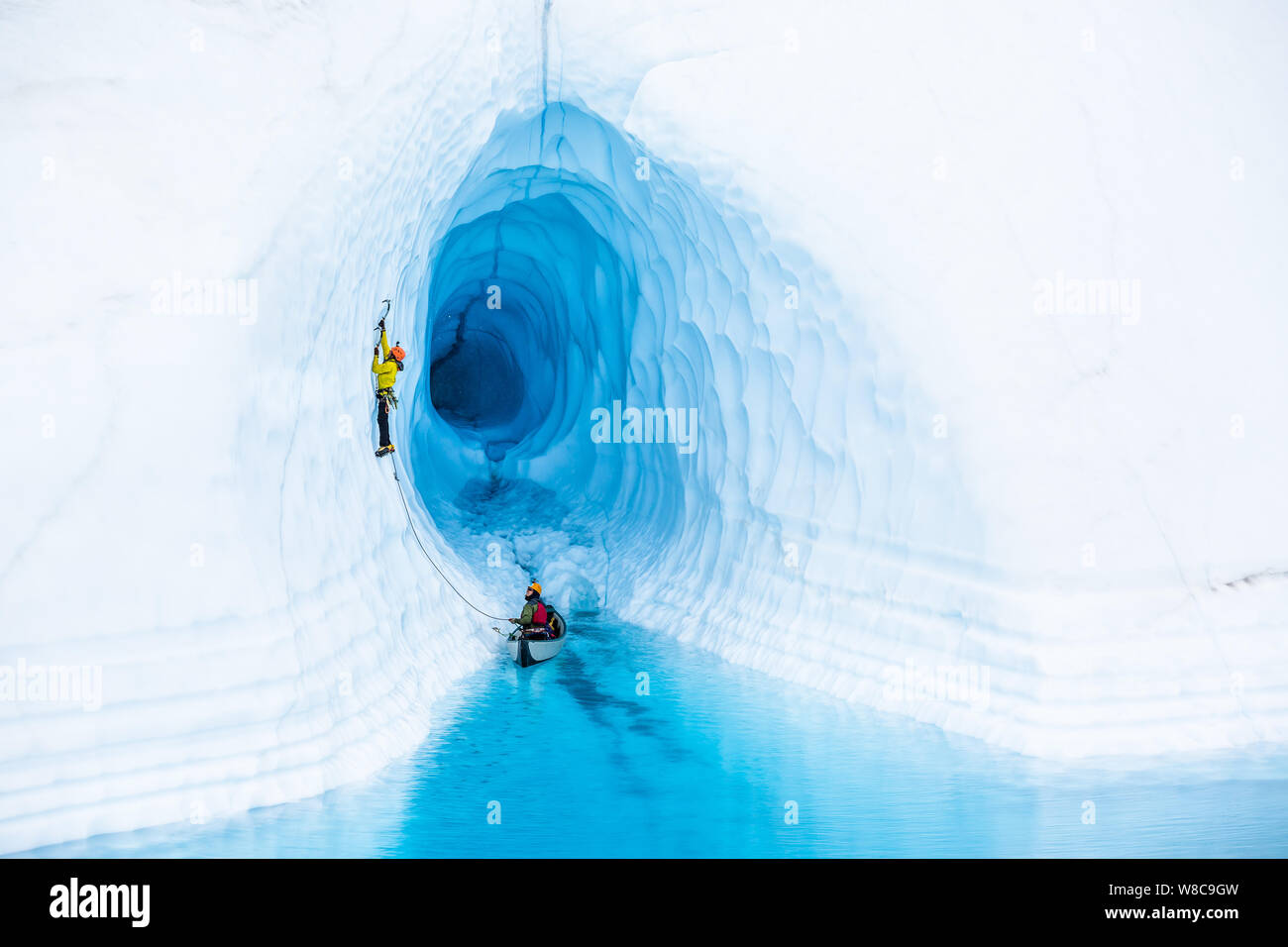 Klettern aus ein Kanu, ein Ice climber führt vom Eingang einer Eishöhle, die von einem blauen Pool auf der Matanuska Gletscher in Alaska überflutet. Stockfoto