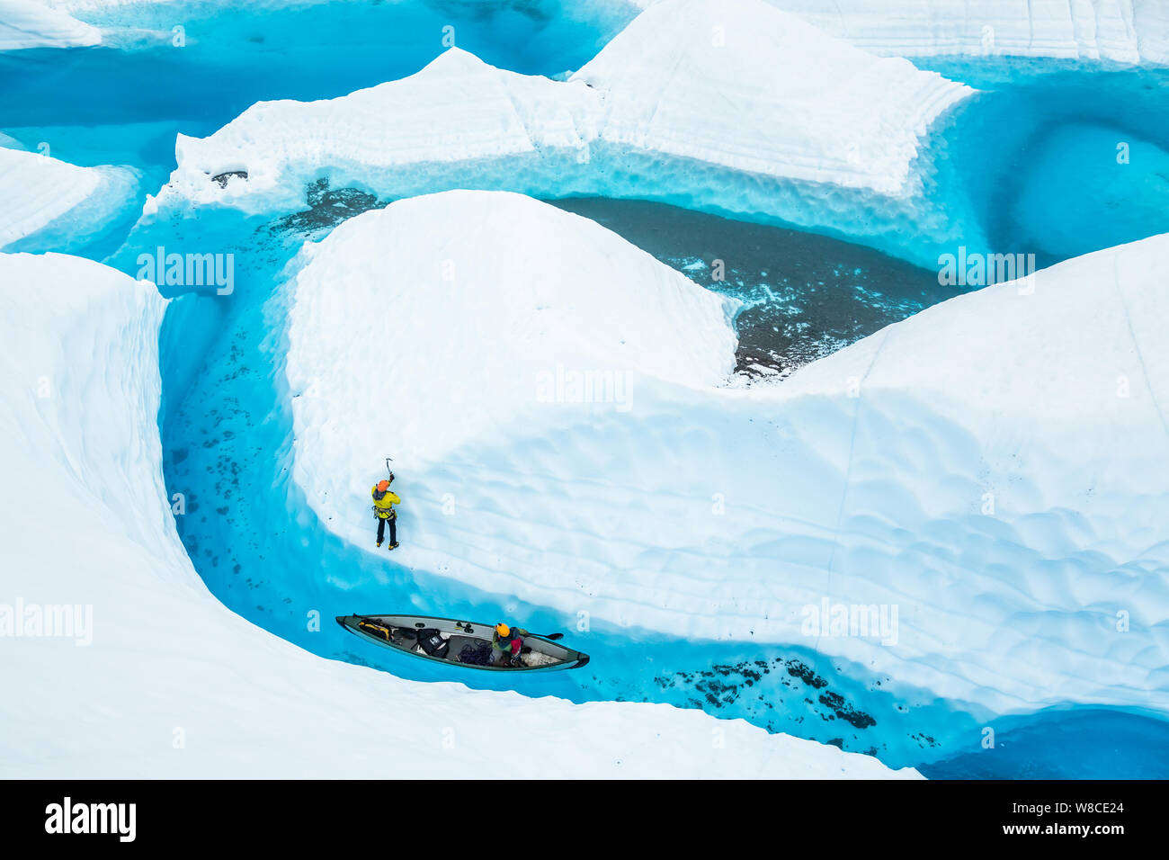Nach dem Klettern aus einem Kanu in einem grossen blauen Pool auf der Matanuska Gletscher, ein junger Mann, der bis Soli ein fin von Eis aus dem Wasser herausragt. Stockfoto