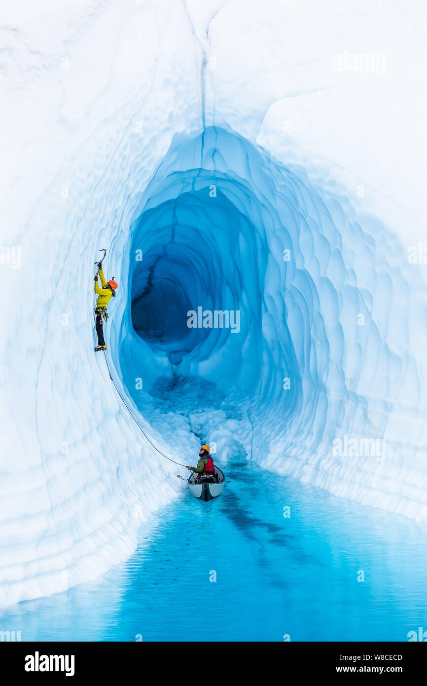 Gletschereis aus einem aufblasbaren Kanu klettern, ein Bergsteiger führt aus einem blauen Pool oder Supraglazialen See. Hinter hte Kletterer ist eine riesige Eishöhle jus Stockfoto