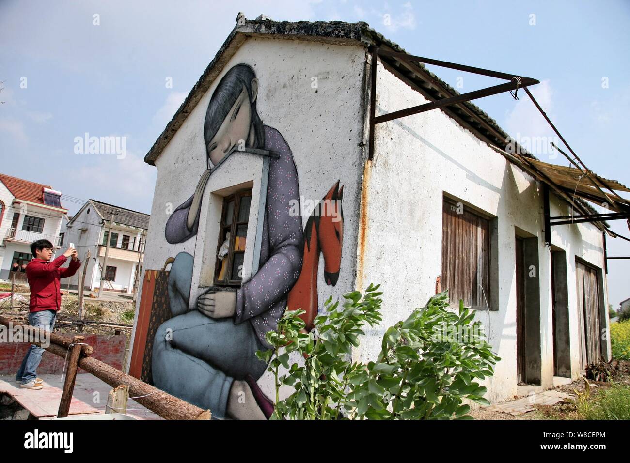 Ein Fußgänger nimmt Fotos auf einer Straße Kunst Malerei des französischen Künstlers Julien Seth Malland an der Wand eines Hauses in Xinyi Dorf Fengjing Stadt in Jins Stockfoto