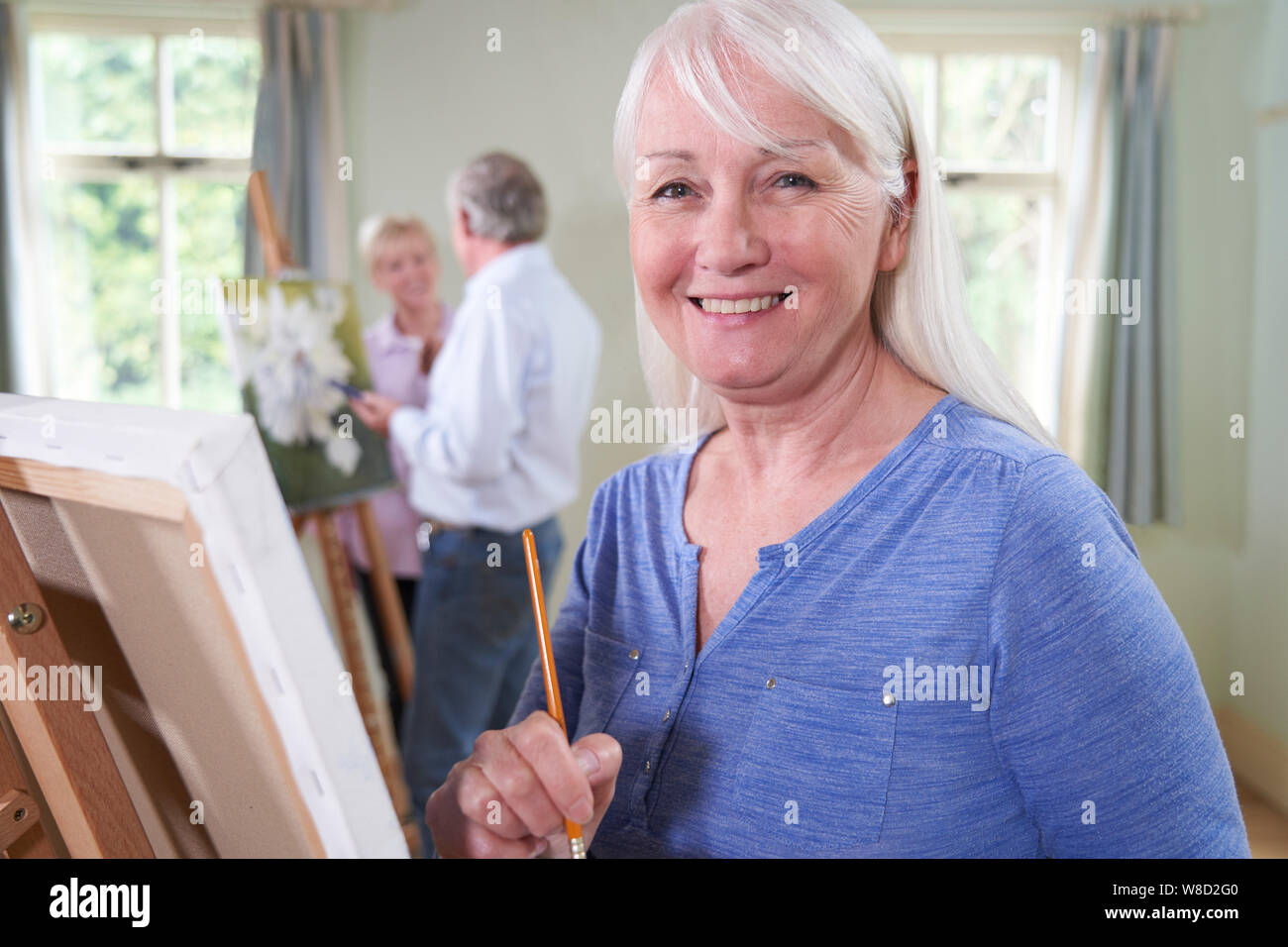 Portrait von Senioren Frau Teilnahme an Malerei Klasse mit Lehrer im Hintergrund Stockfoto