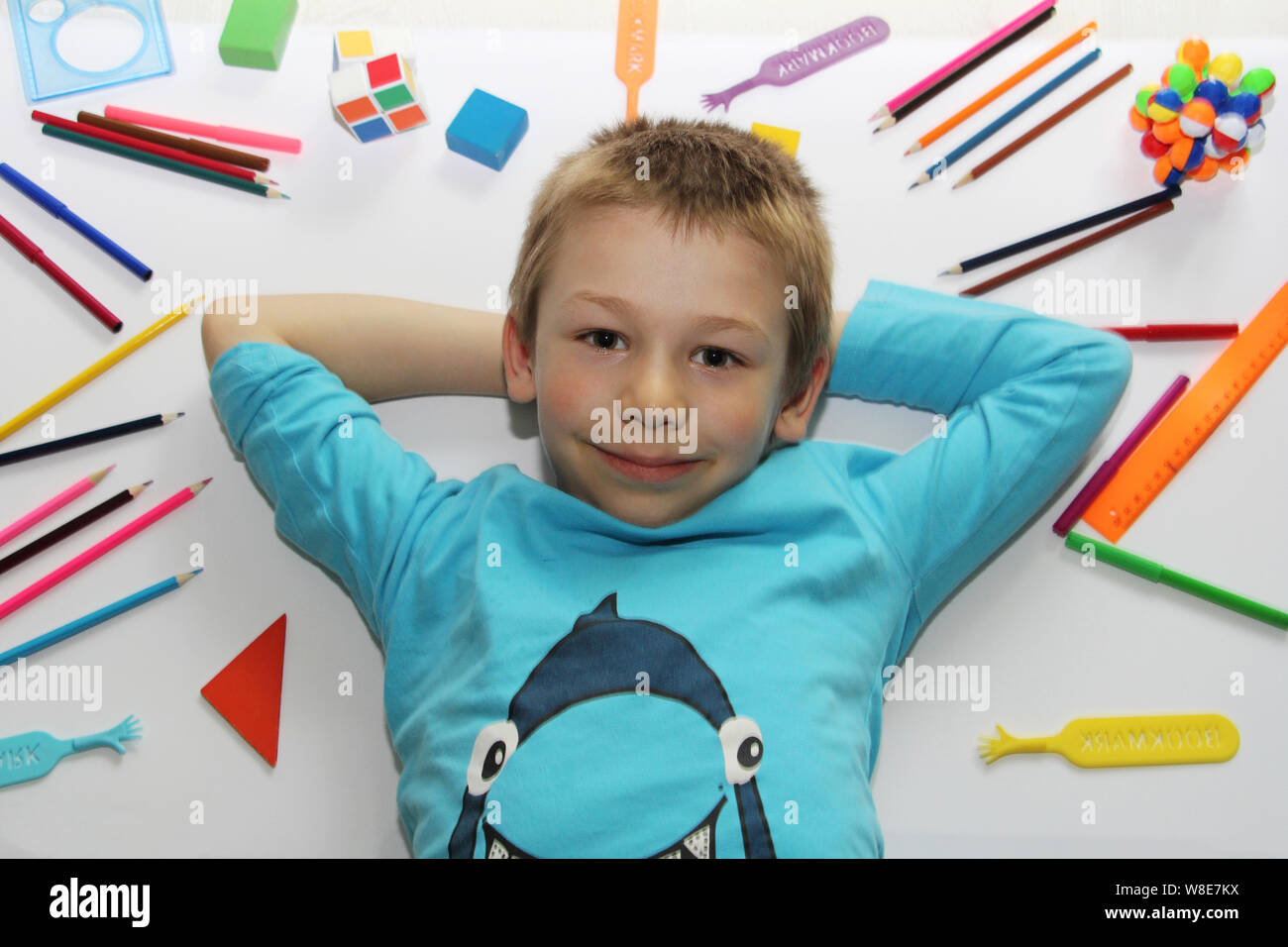 Der Junge liegt auf einem weißen Hintergrund, Schulsachen sind in der näheren Umgebung verstreut. Der Junge ist immer bereit, um in die Schule zu gehen. Lineale, Kugelschreiber, Bleistifte. Das Kind r Stockfoto