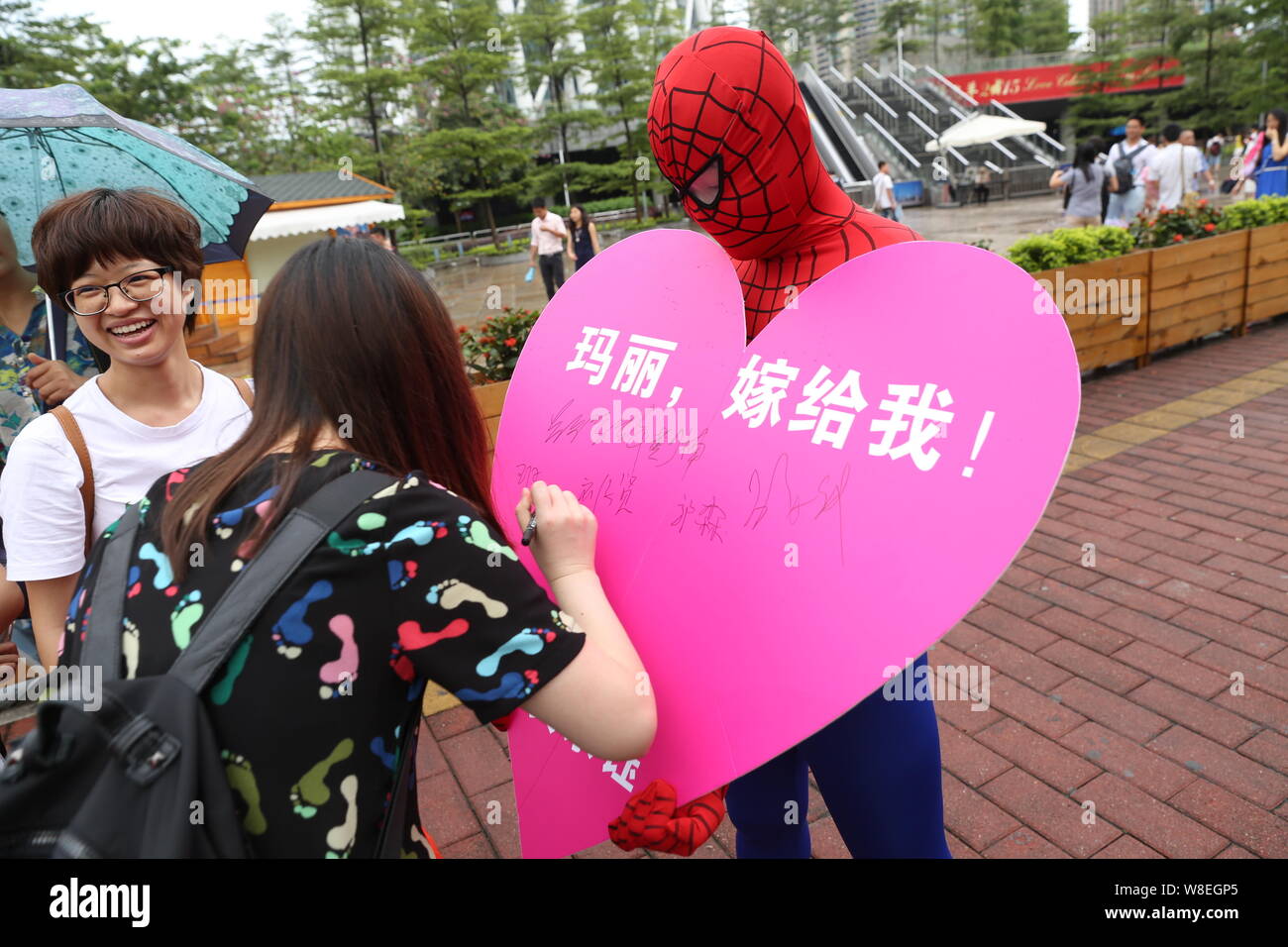 Ein Mann, gekleidet in der Spider-man Kostüm sammelt Unterschriften von 520 Fremden ihm ihren Segen auf einem Herzen zu geben-förmigen Zeichen in der Stadt Guangzhou, Sou Stockfoto