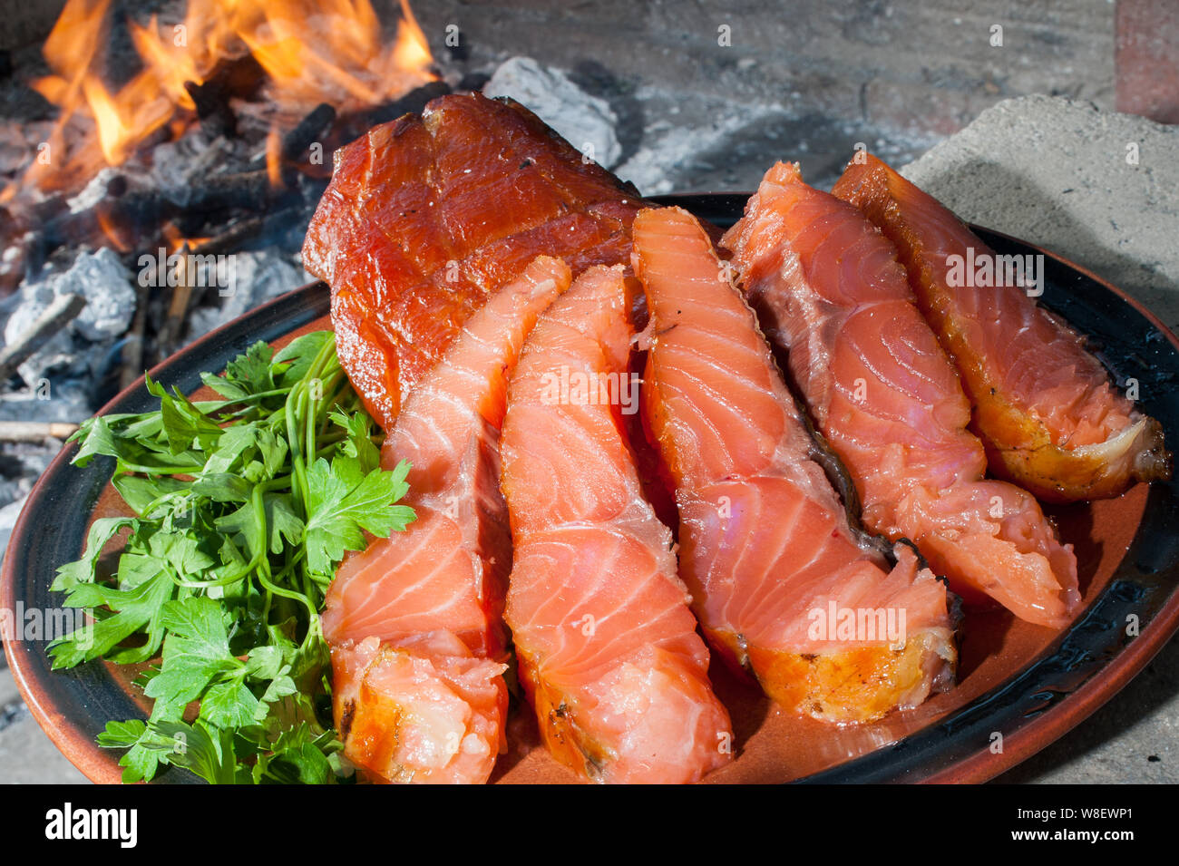 Die Platte von geräuchertem Lachs auf dem Holzkohlegrill mit dem Verbrennen von Kohle im Hintergrund Stockfoto