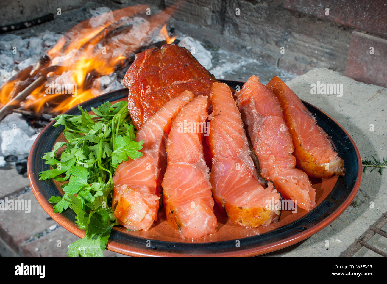 Die Platte von geräuchertem Lachs auf dem Holzkohlegrill mit dem Verbrennen von Kohle im Hintergrund Stockfoto