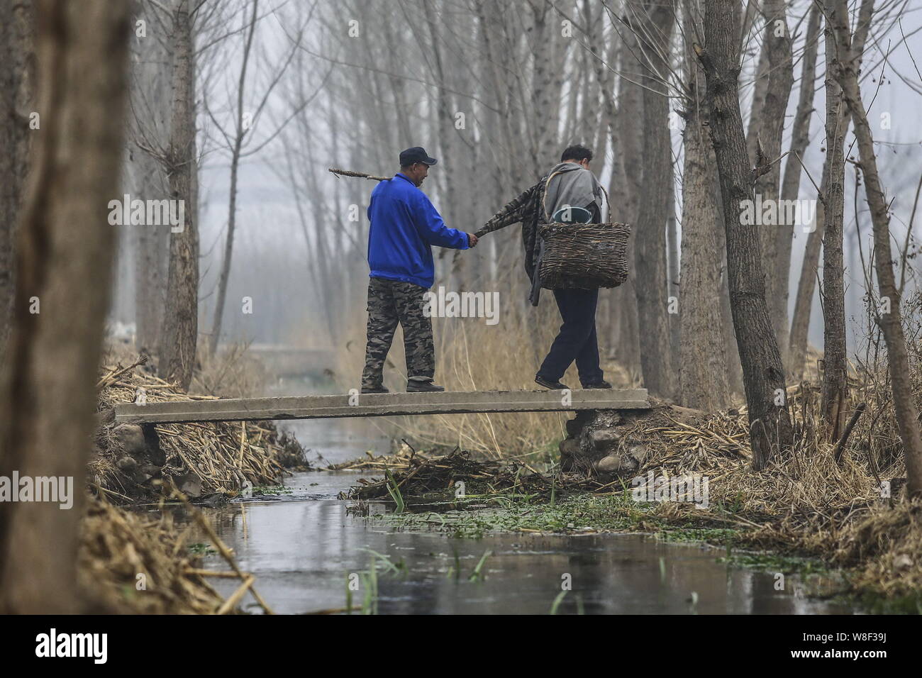 Armlose Chinese Jia Wenqi, rechts, führt seinen blinden Freund Jia Haixia mit einem Ärmel seines Mantels an einem Kanal, der über eine Brücke auf dem Weg kreuz Stockfoto