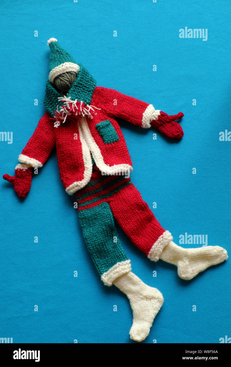 Blick von oben auf die Santa Kleidung mit Zubehör wie Handschuhe, Mütze, Schal, Socken in den Farben Weiß, Rot und Grün aus Garnen auf blauem Hintergrund stricken, kleine Verzierungen Stockfoto