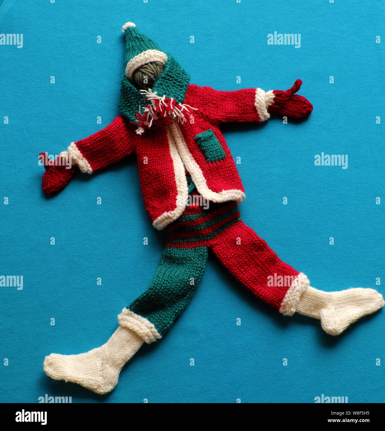 Blick von oben auf die Santa Kleidung mit Zubehör wie Handschuhe, Mütze, Schal, Socken in den Farben Weiß, Rot und Grün aus Garnen auf blauem Hintergrund stricken, kleine Verzierungen Stockfoto