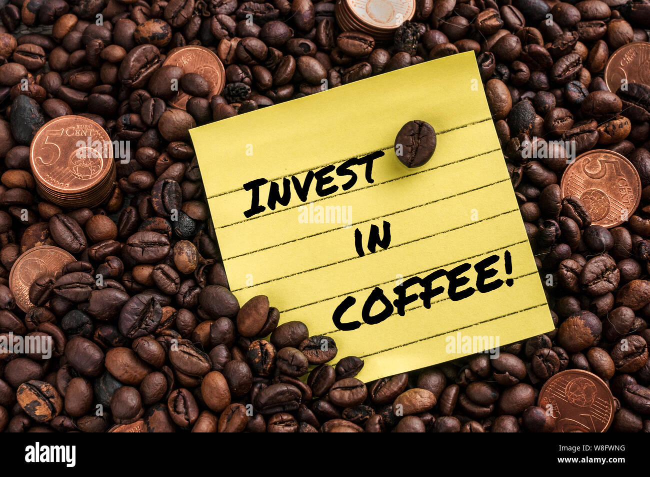 Euro Münze über frischen Kaffee gerösteten Bohnen und ein gelber Hinweis mit dem Satz: in Kaffee investieren Stockfoto