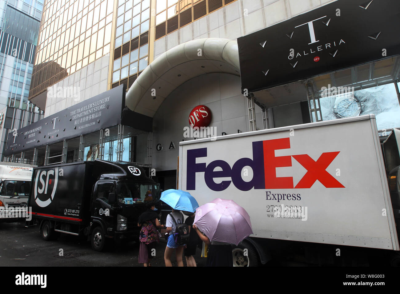 ---- Fußgänger vorbei einen FedEx Express Lieferung Auto und ein SF Express Lieferung Auto in Hongkong, China, 18. Juli 2014. FedEx Corp. ist Du zu kaufen Stockfoto