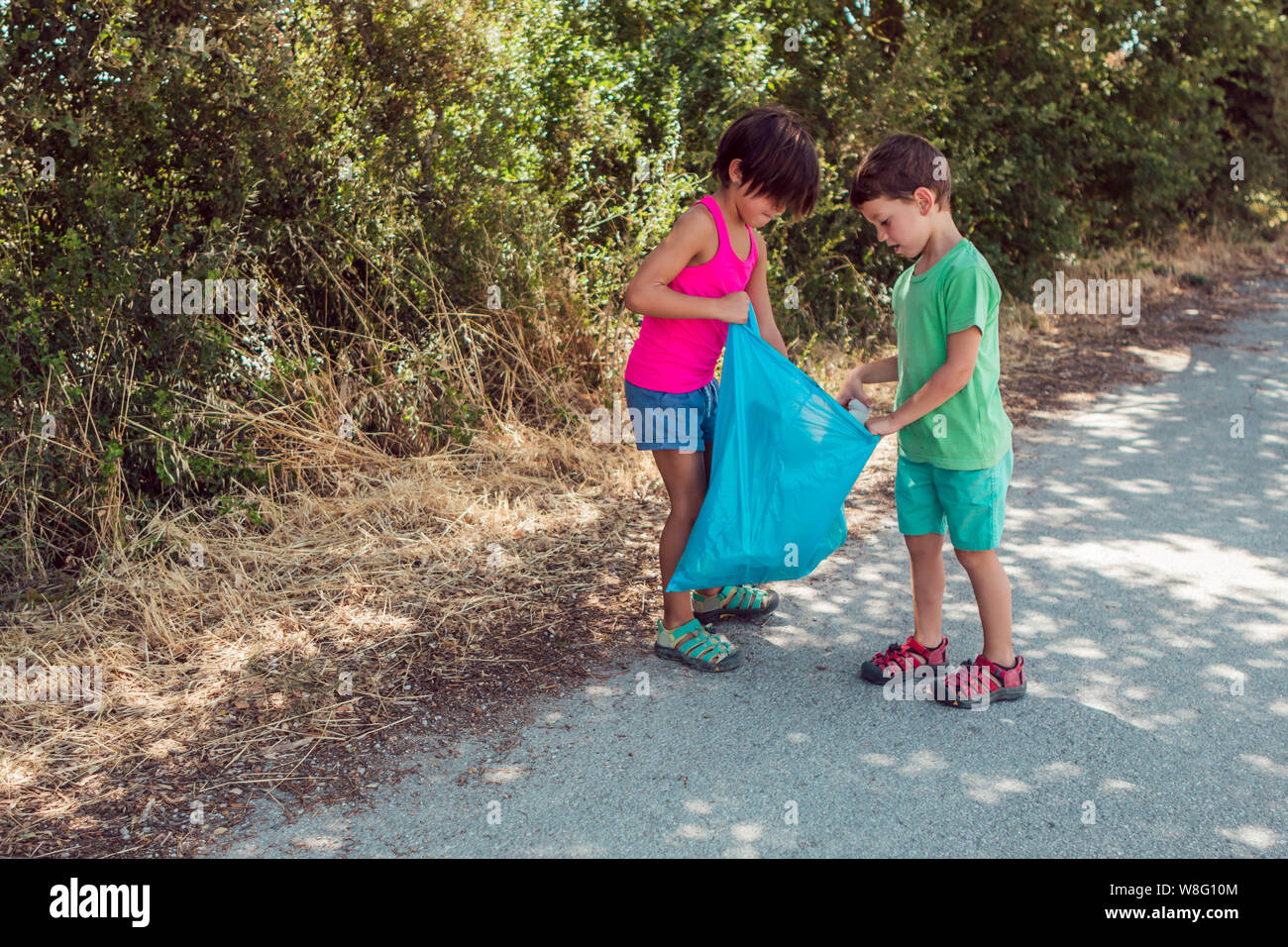 Sie Kinder Wurf in eine blaue Plastiktüte im Freien. Ökologiekonzept Stockfoto