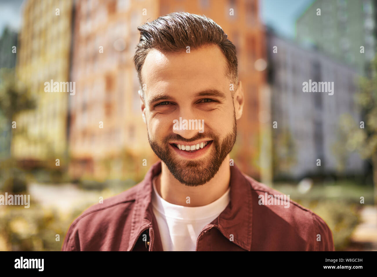 Hello Portrait von glücklich attraktiven Mann mit Stoppeln lächeln und Blick auf die Kamera, während auf der Straße stehen. Schönheit für Männer. Glück. Positive Emotionen Stockfoto