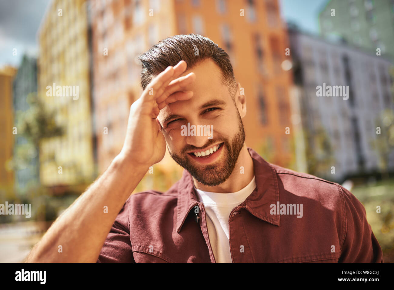 Sonnentag Porträt von glücklich attraktiven Mann mit Stoppeln lächeln und Blick auf die Kamera, während auf der Straße stehen. Schönheit für Männer. Glück. Positive Emotionen Stockfoto